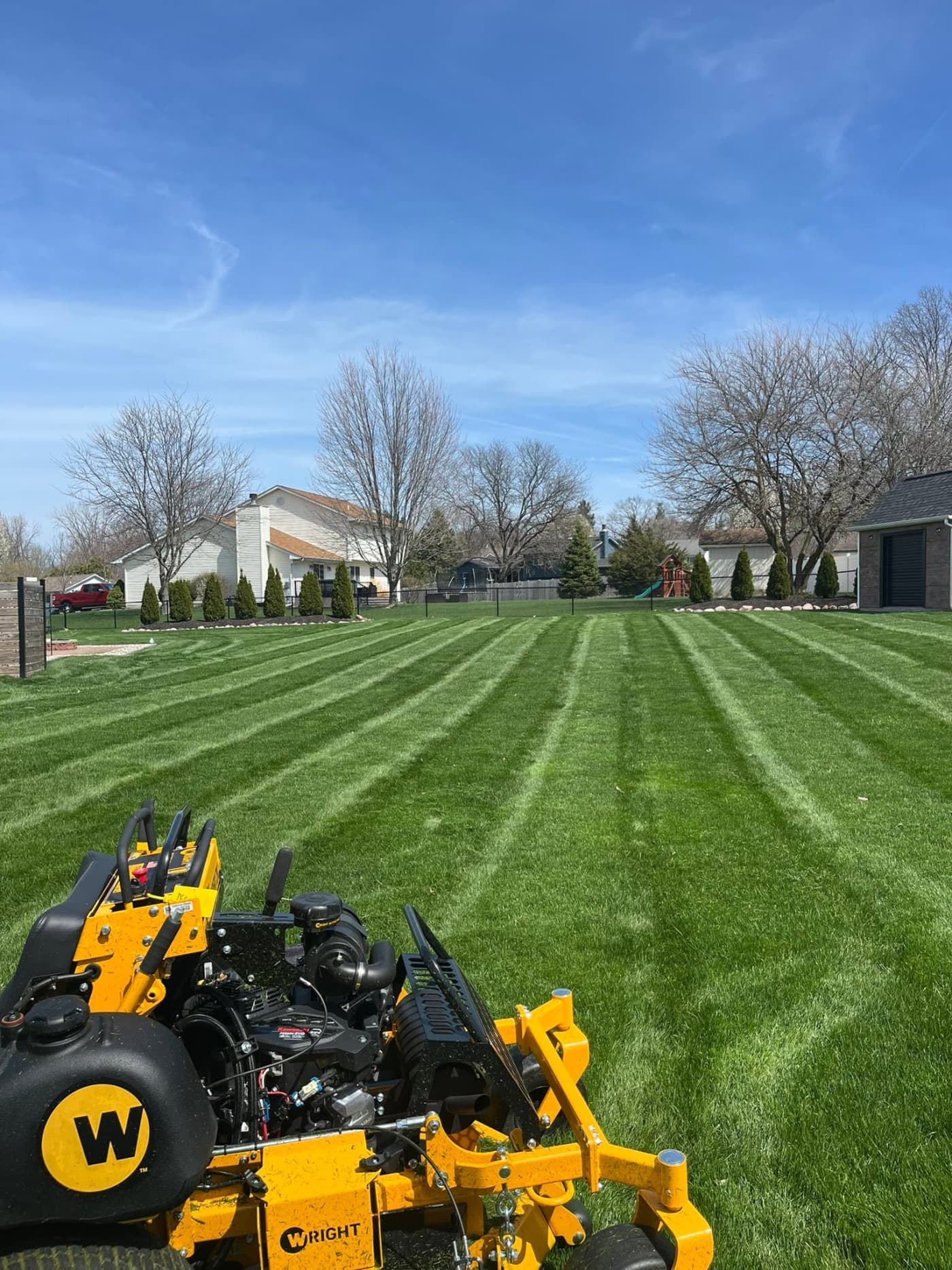 Freshly striped lawn beside a stand-on commercial mower